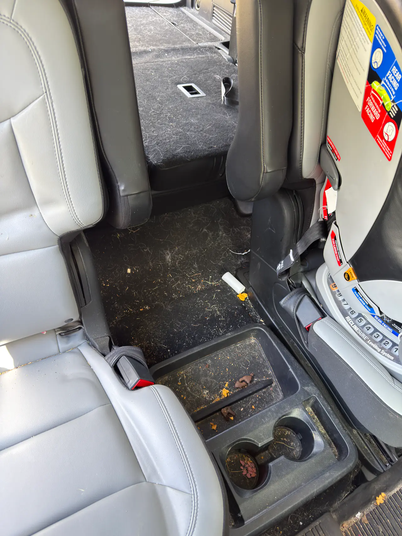 Before an interior detail: crumbs and debris across an SUV's second-row console and floor