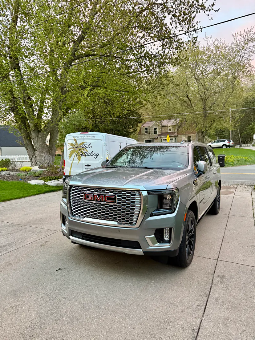 Silver GMC Yukon Denali after a mobile detail, the Lifestyle Detailing van in the driveway behind it