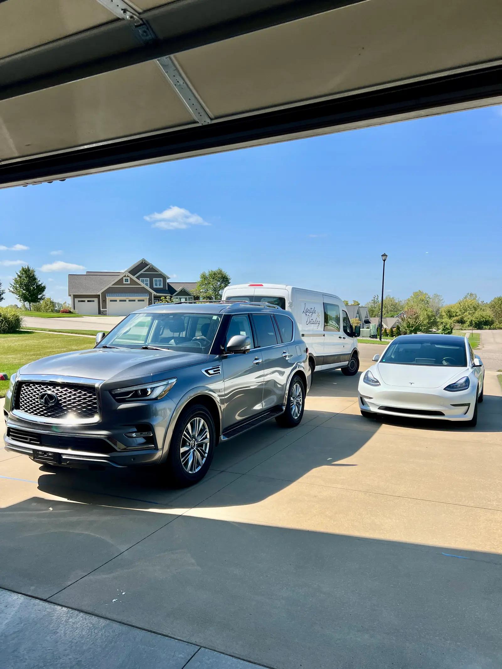 Infiniti QX80 and Tesla Model 3 detailed in the same driveway, seen from inside the garage