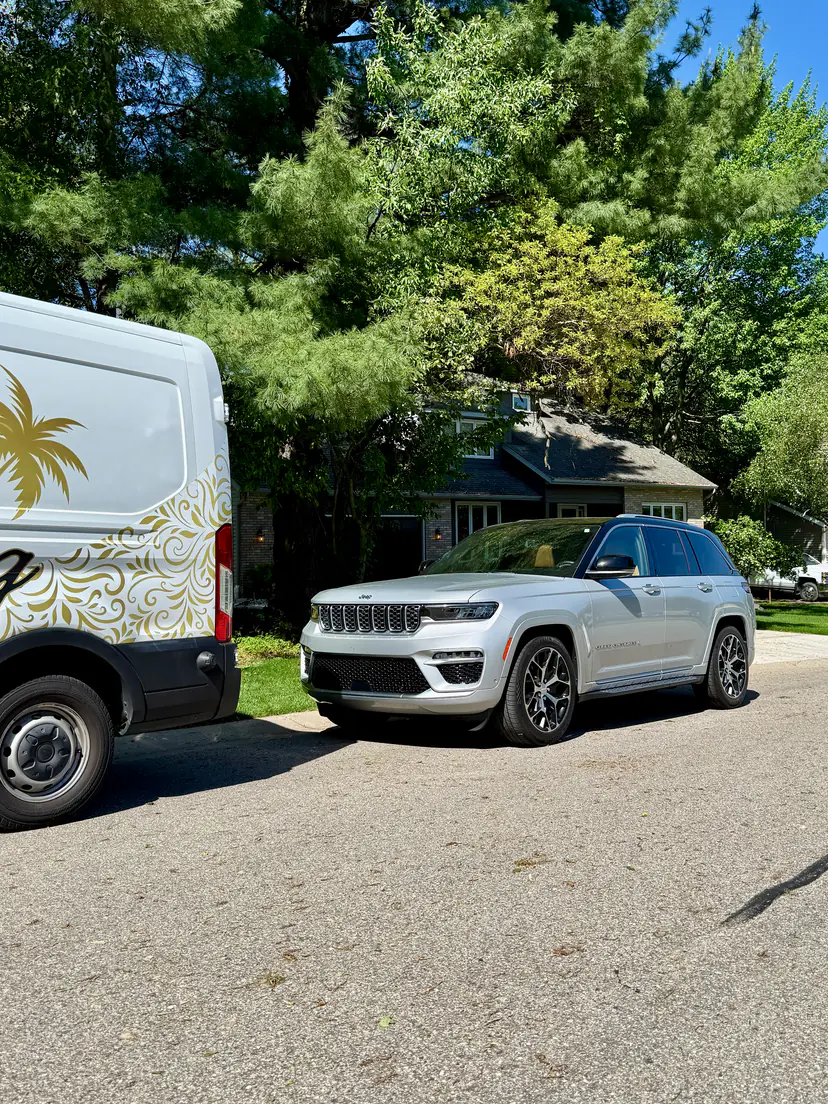 Silver Jeep Grand Cherokee after a mobile detail on a tree-lined street in Wyoming, Michigan, the Lifestyle Detailing van beside it
