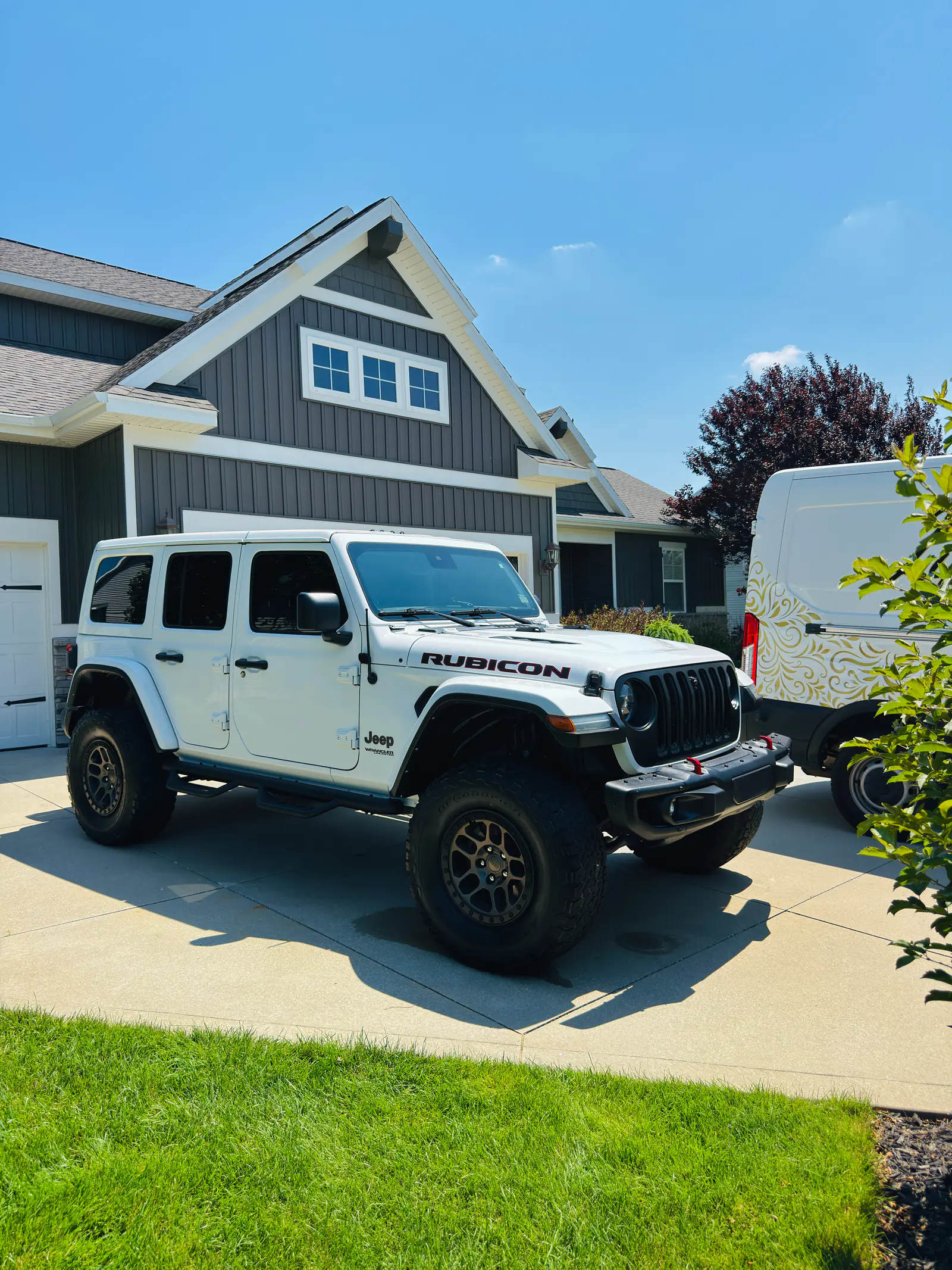 White Jeep Wrangler Rubicon after an exterior detail in front of a dark board-and-batten home