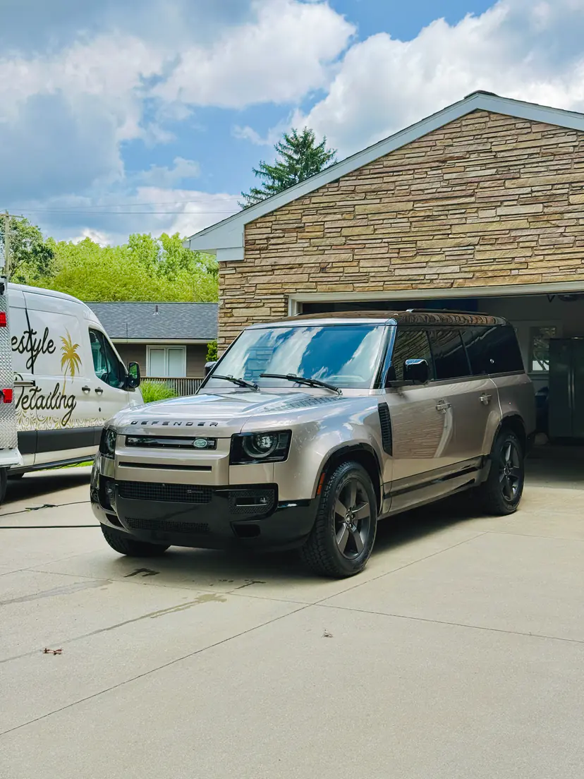 Land Rover Defender 110 freshly detailed in the driveway of a stone home, the Lifestyle Detailing van behind it