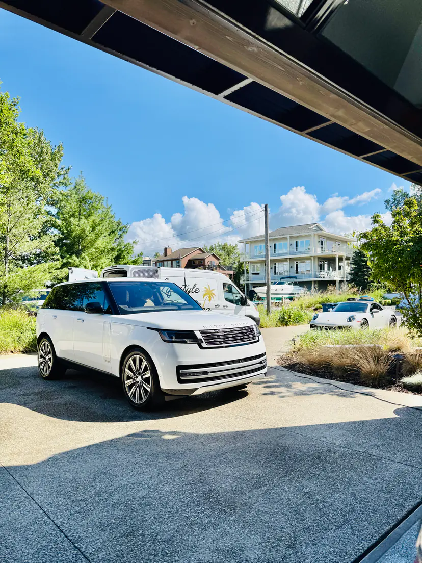 White Range Rover gleaming after a mobile exterior detail, framed under a timber garage eave with the Lifestyle Detailing van and a Porsche 911 behind it