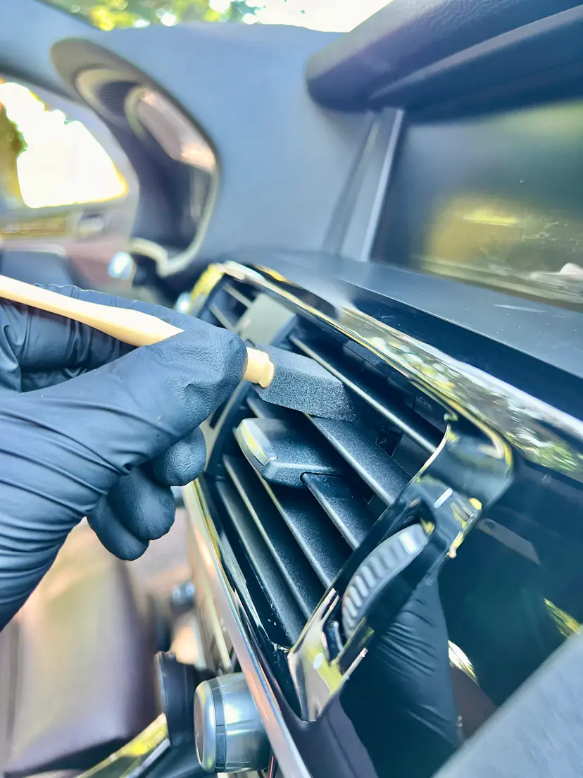 Gloved hand easing a foam swab into a BMW air vent during a mobile interior detail in Grand Rapids Township, Michigan