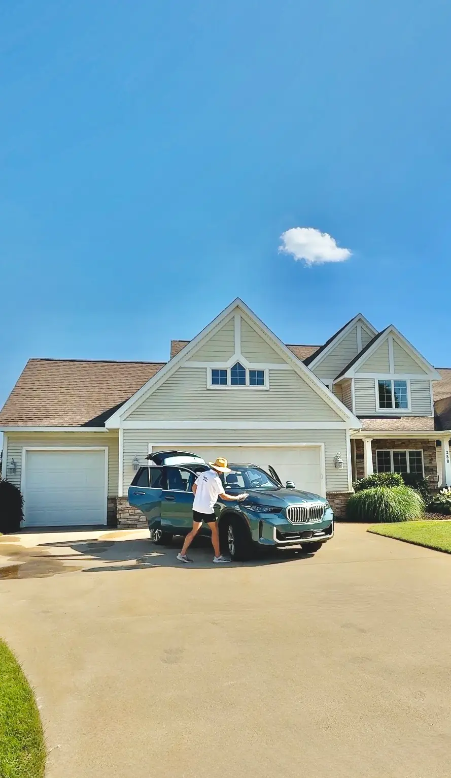 Chase Shooltz detailing a teal BMW X5 in a customer's driveway under a clear blue sky