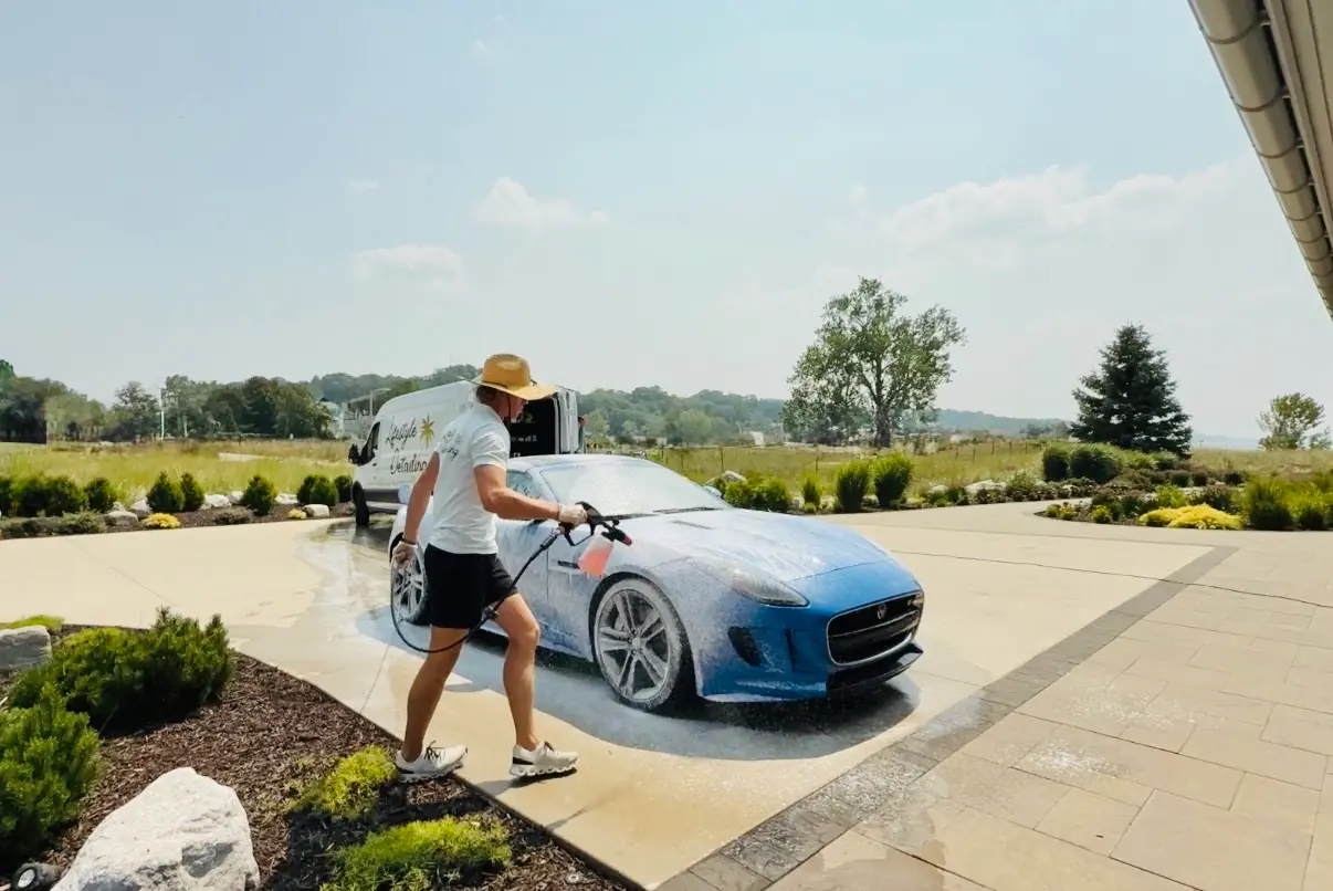 Chase Shooltz foaming a blue Jaguar F-Type during a mobile hand wash, the Lifestyle Detailing van behind