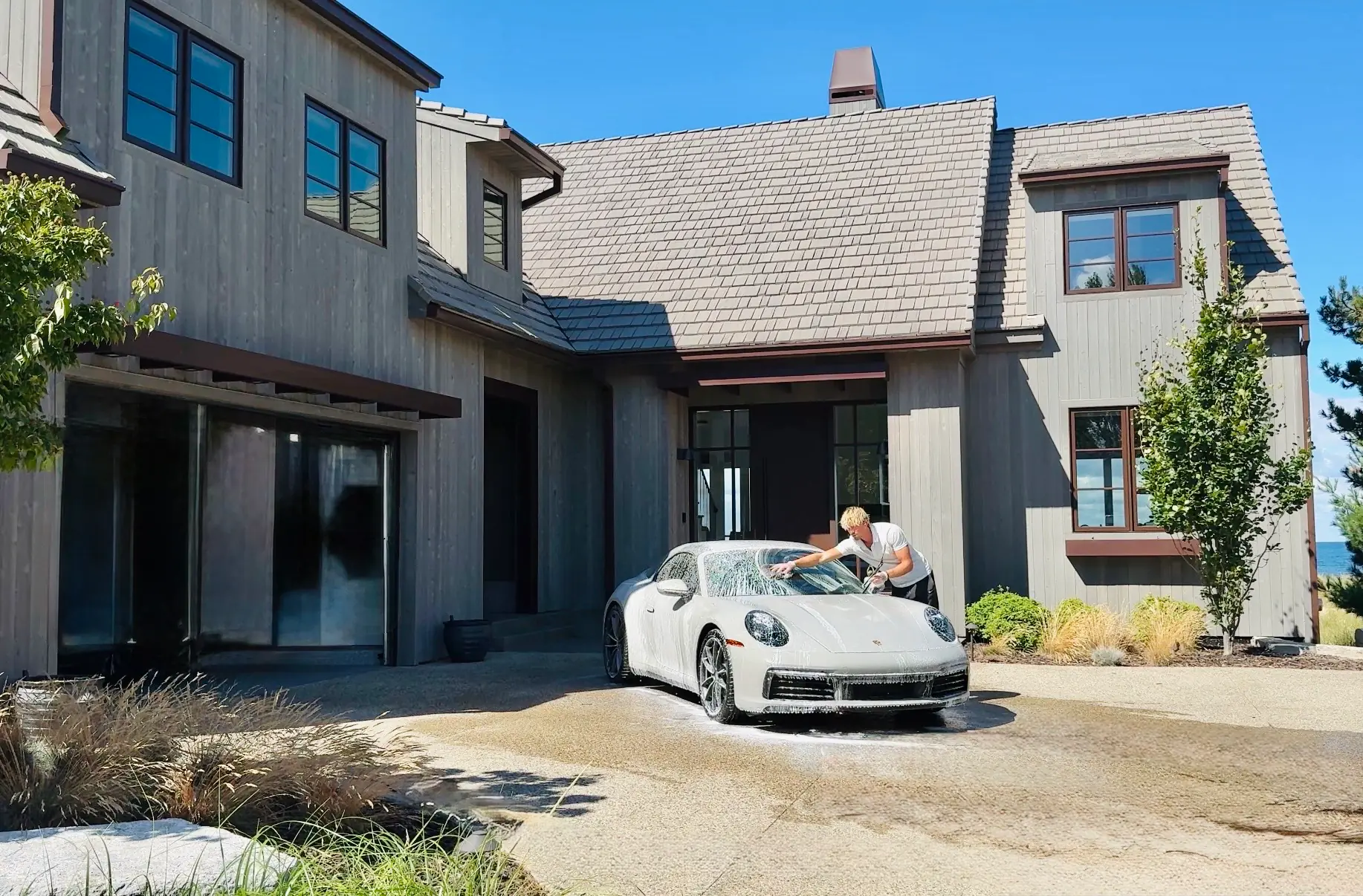 Chase Shooltz hand-drying a white Porsche 911 after a hand wash in front of a modern farmhouse
