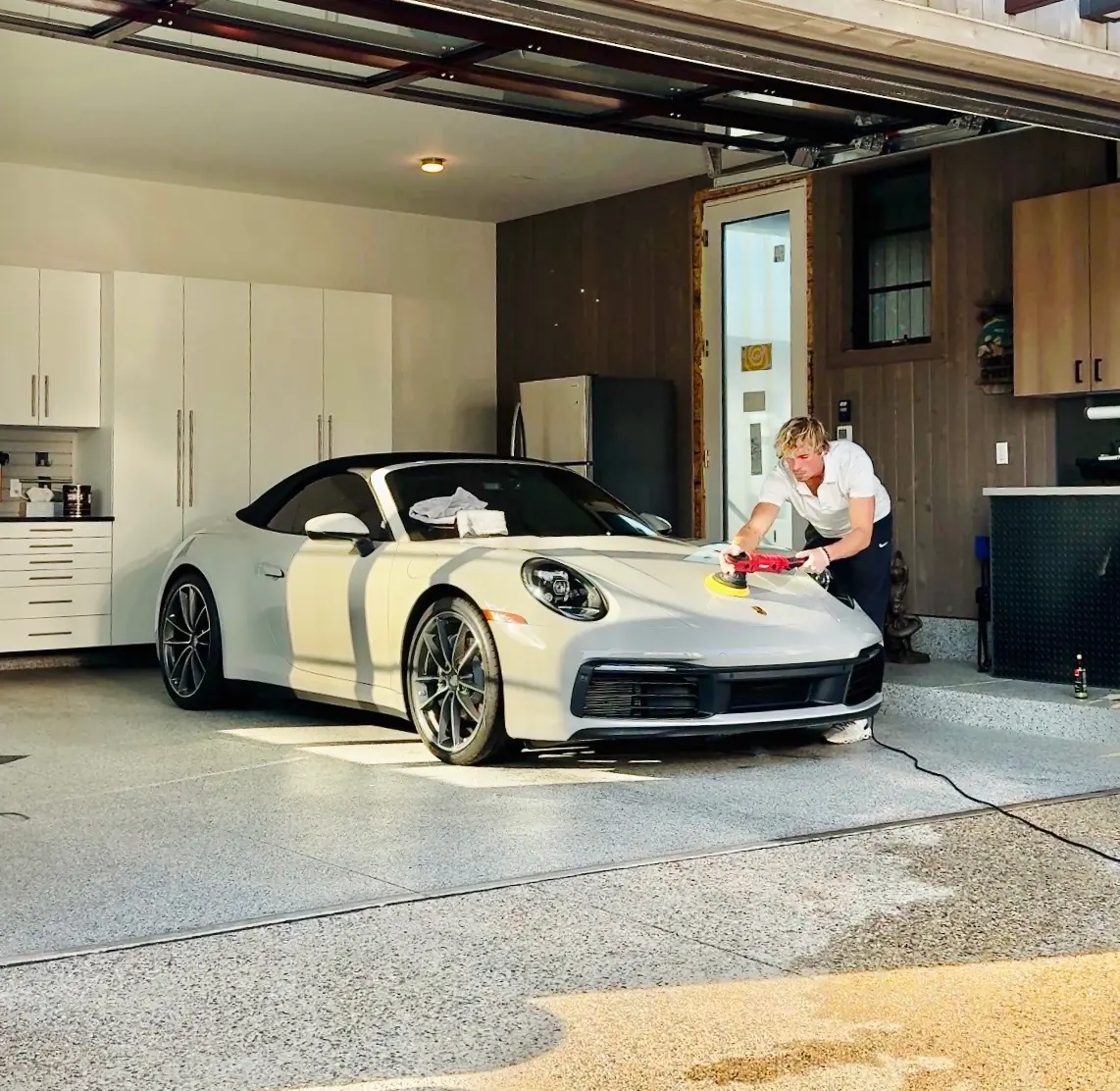 Chase S. machine-polishing a white Porsche 911 in a home garage during paint correction