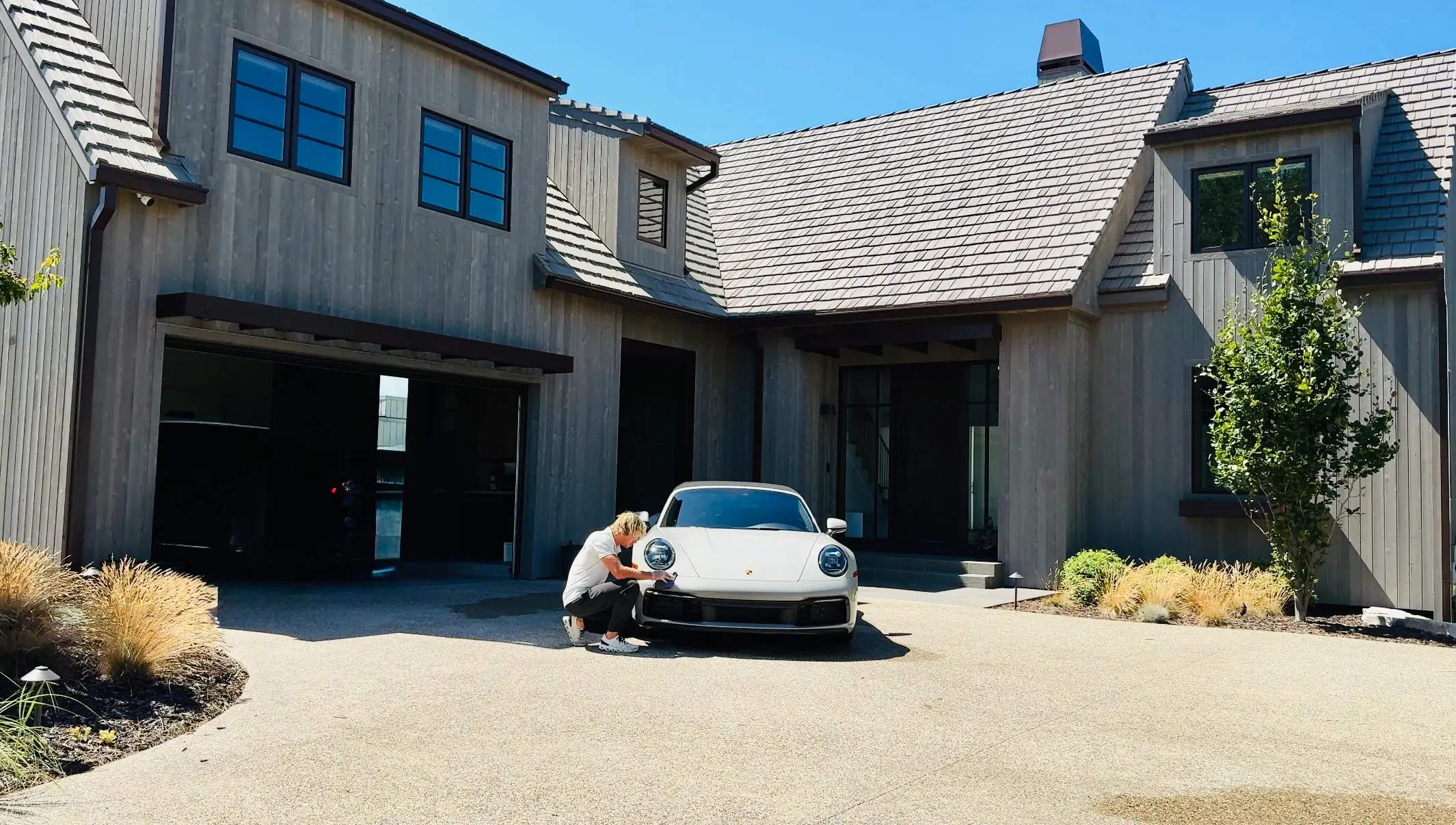 Chase Shooltz detailing a white Porsche 911 in the driveway of a modern farmhouse during a mobile full detail