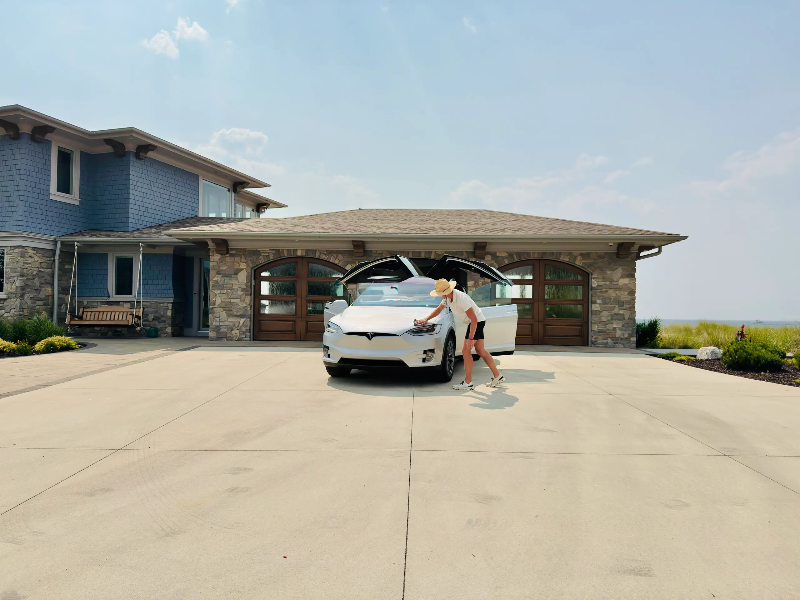 Chase Shooltz detailing a white Tesla Model X with its falcon-wing doors open at a customer's stone home