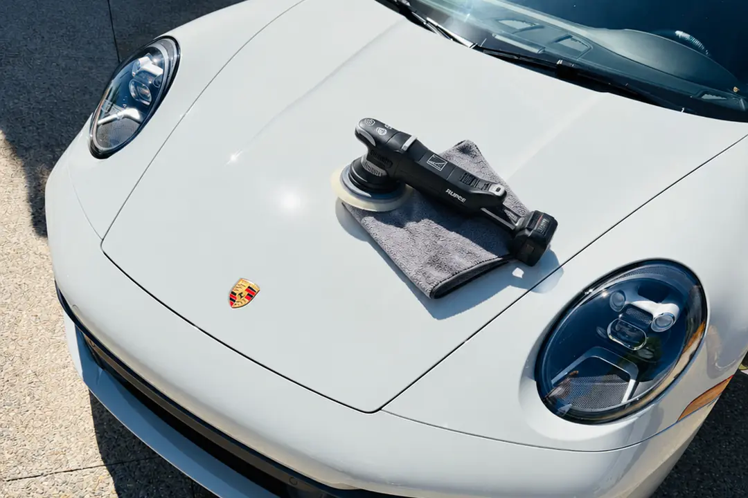 A polisher and a microfiber towel resting on the hood of a white Porsche 911 Cabriolet during a Deluxe Detail