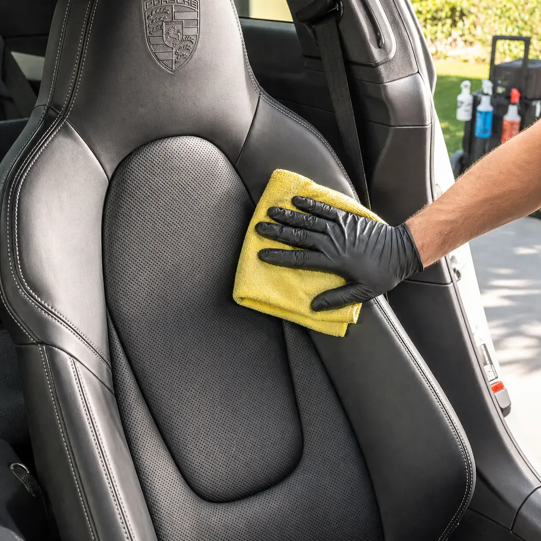A microfiber towel wiping a Porsche leather seat during an Interior Refresh