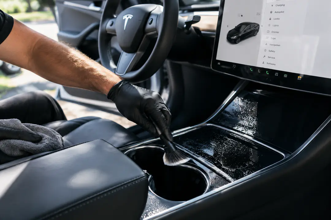 A detailing brush cleaning a Tesla's center console during a Signature Interior Detail